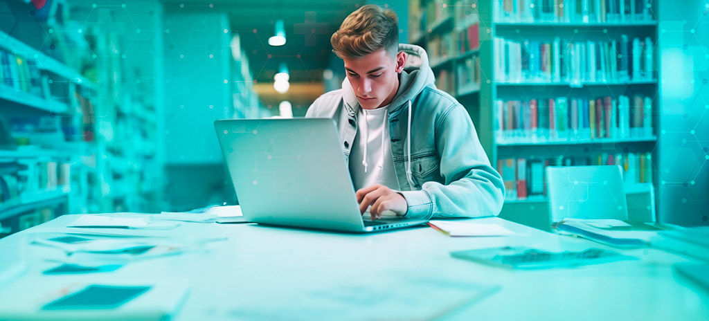 Jovem adolescente branco com moletom sentado em uma cadeira em uma biblioteca com notebook buscando na internet como estudar para medicina do zero