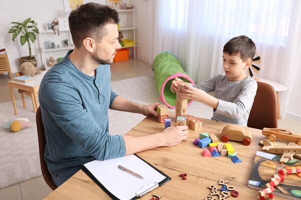 Psicólogo fazendo sessão de terapia com blocos educativos com paciente com autismo em consultório