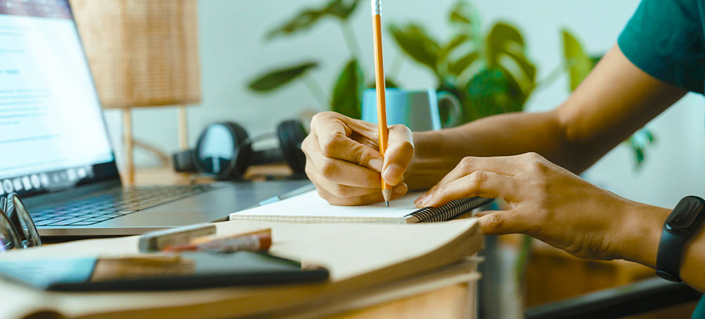 Homem jovem estudando, com lápis, caderno e computador, os assuntos mais cobrados do Enem