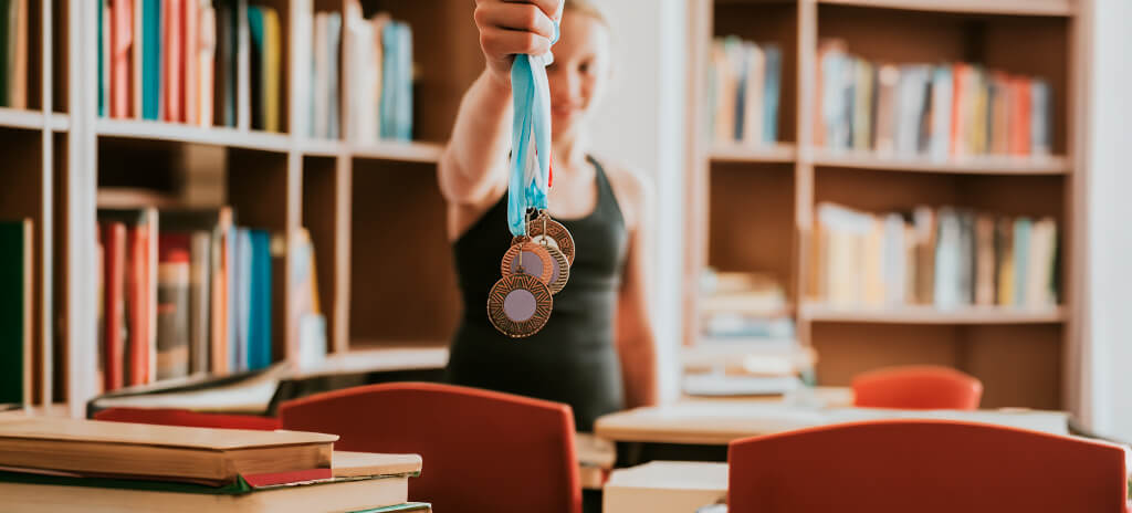 Adolescente em biblioteca segurando medalhas de olimpíadas científicas que dão acesso às vagas olímpicas em universidades brasileiras