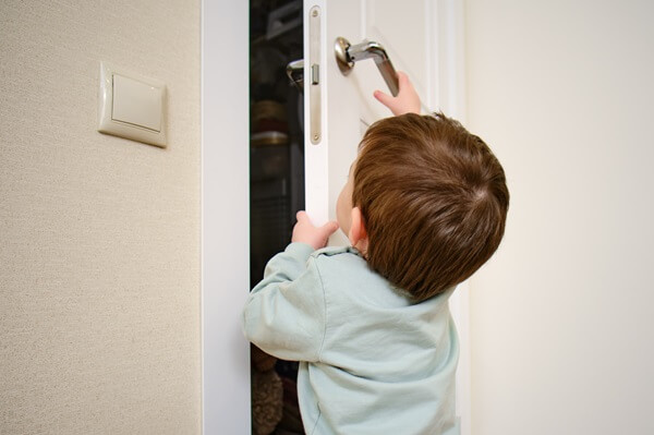 Menino segurando na porta de madeira e puxando a maçaneta de metal