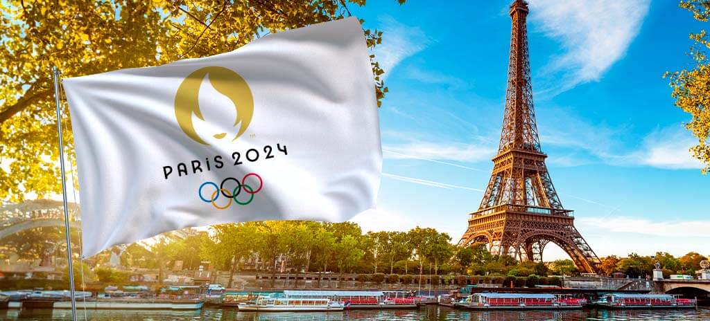 Vista da Torre Eiffel em Paris ao fundo. Na frente, uma bandeira dos Jogos Olímpicos de 2024
