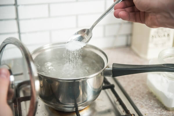 Mão segurando colher de sal para colocar em panela com água fervente