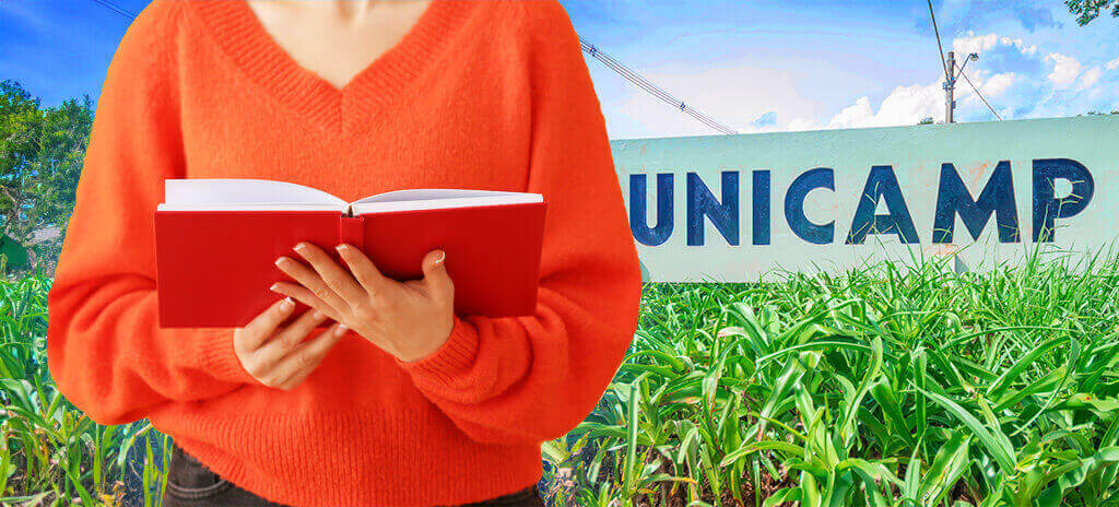 Mulher de blusa laranja segurando livro e lendo resumo dos livros Unicamp em frente a Unicamp