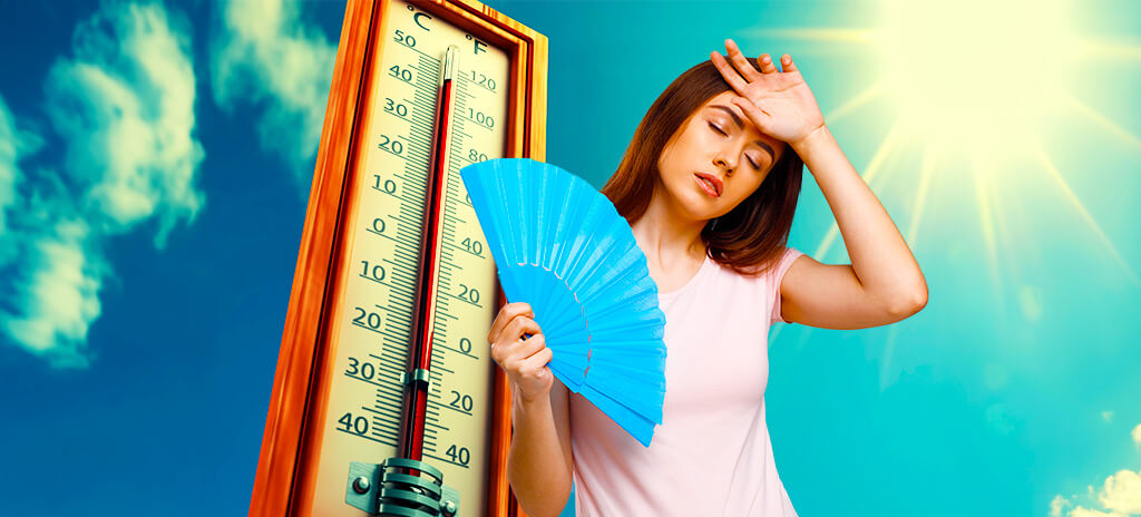 Mulher se abanando com leque para diminuir sensação térmica e calor e termômetro atrás marcando altas temperaturas
