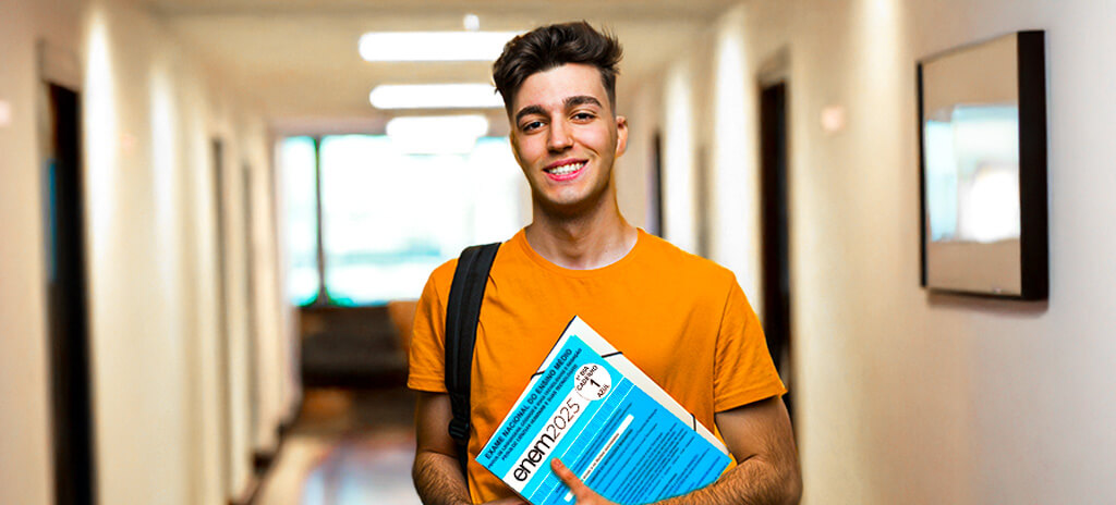Vestibulando em corredor de universidade segurando caderno azul do Enem 2025 nos braços