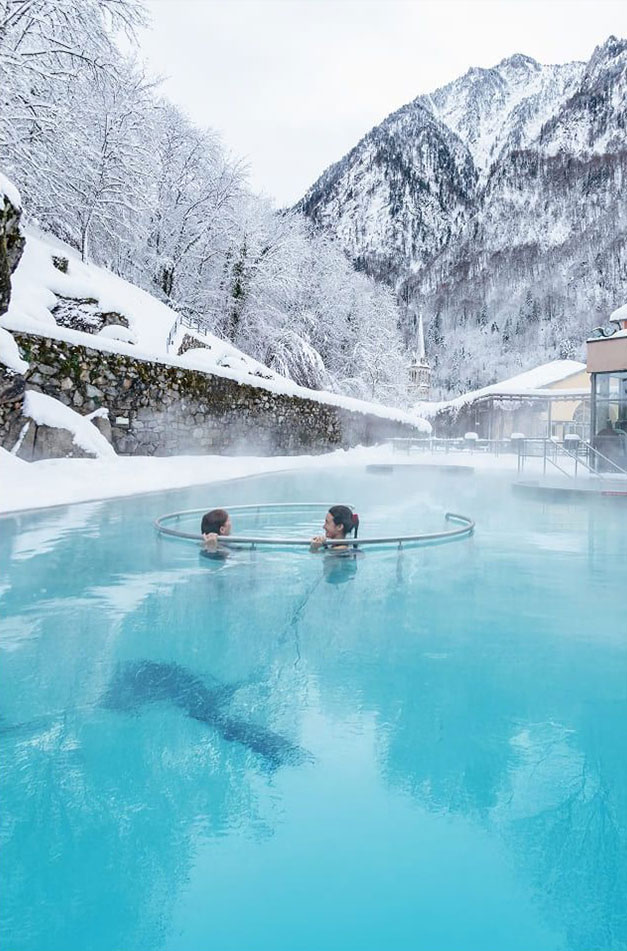 Two people relaxing in an outdoor bath in the snow at Bains du Rocher in Cauterets