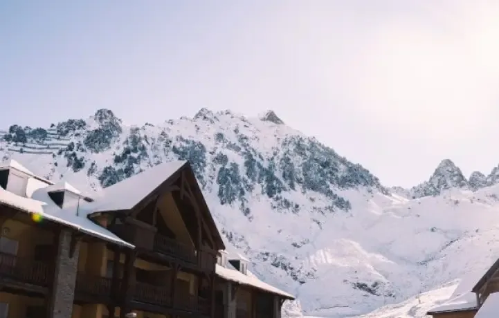 A mountain lodge with snow on the roof, at the feet of the mountains