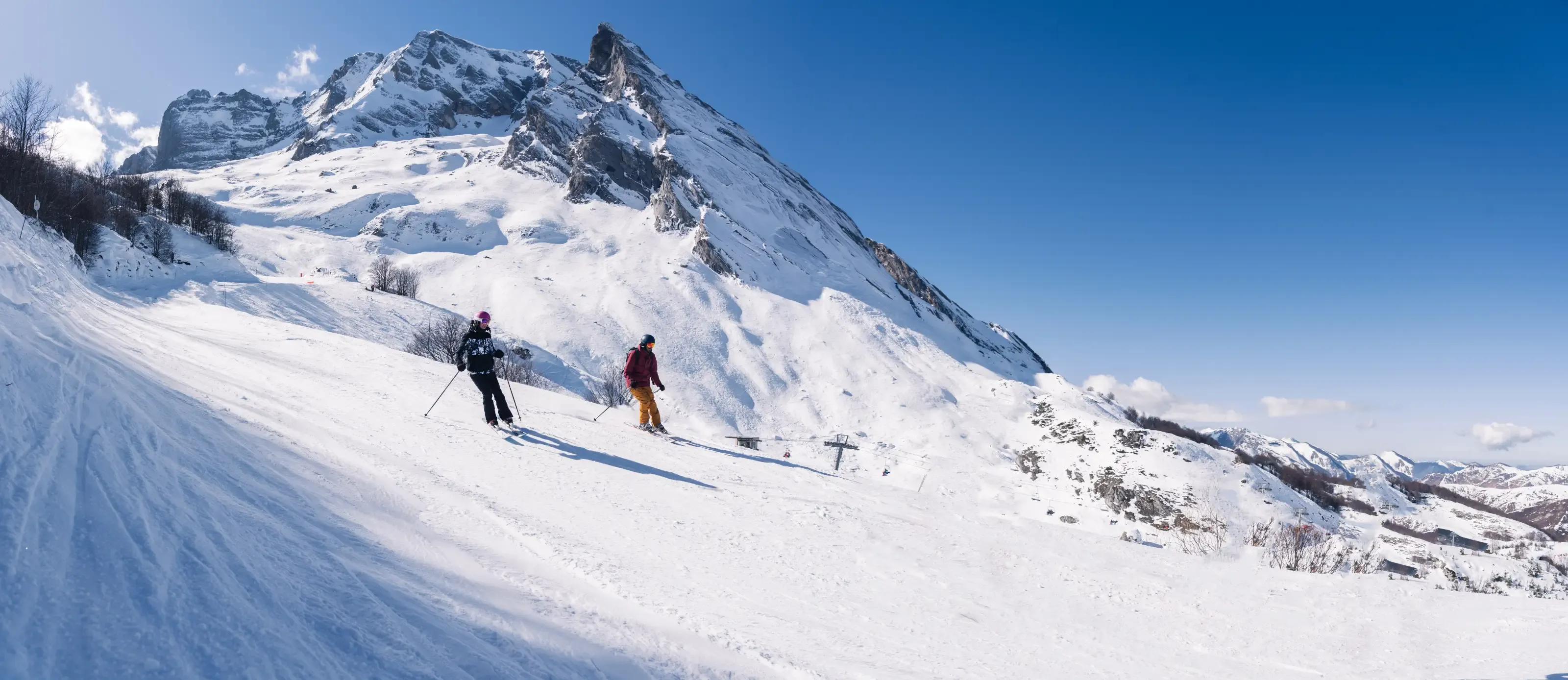 Deux skieurs descendants une piste de la station de Gourette avec les falaises du Pic du Ger en fond