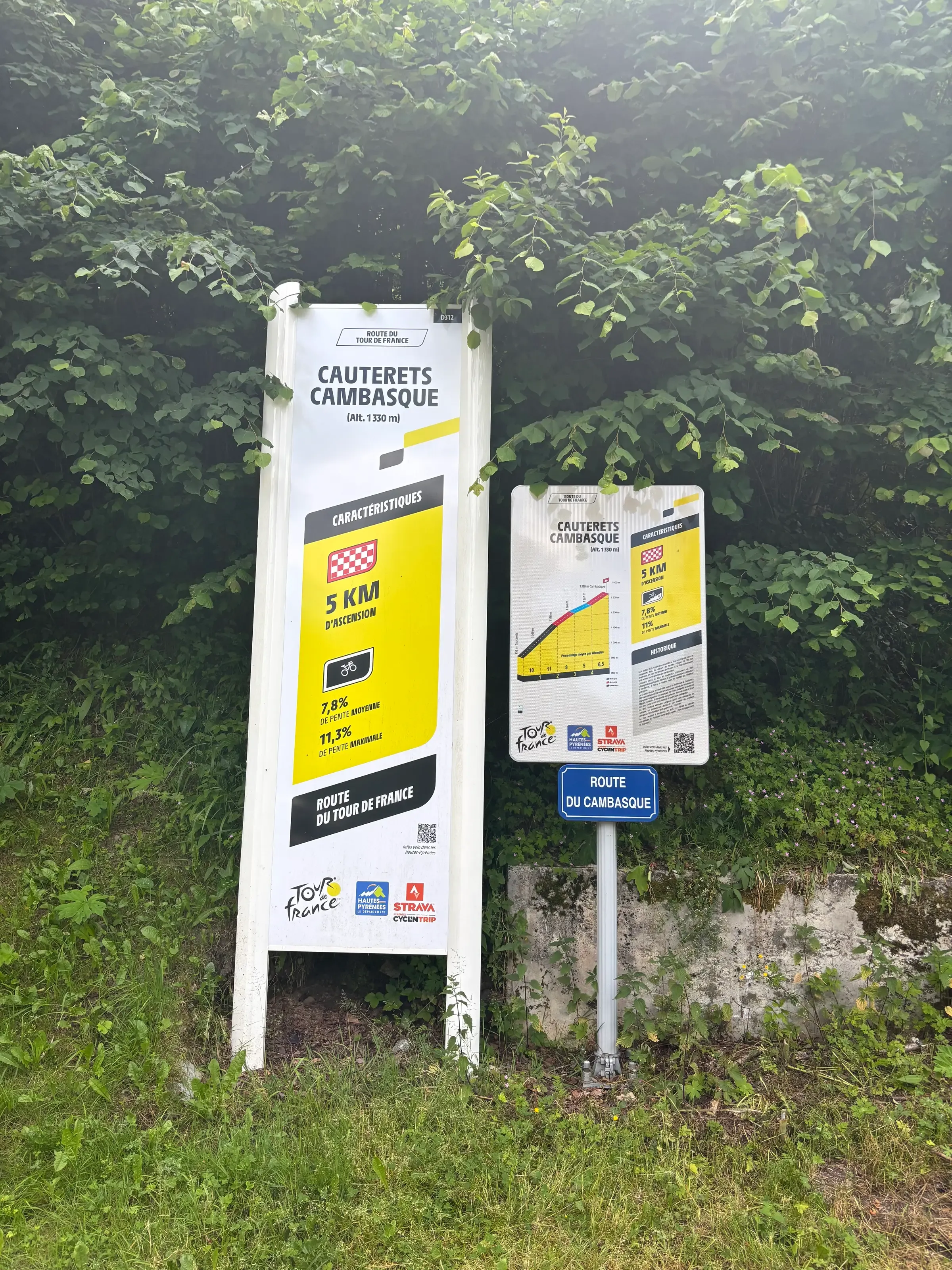 Deux panneaux d'information du Tour de France détaillent les caractéristiques de l'ascension cycliste de Cauterets-Cambasque, installés devant une végétation verdoyante.