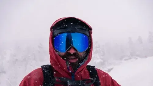 visage d'un skieur avec masque et capuche sous la neige