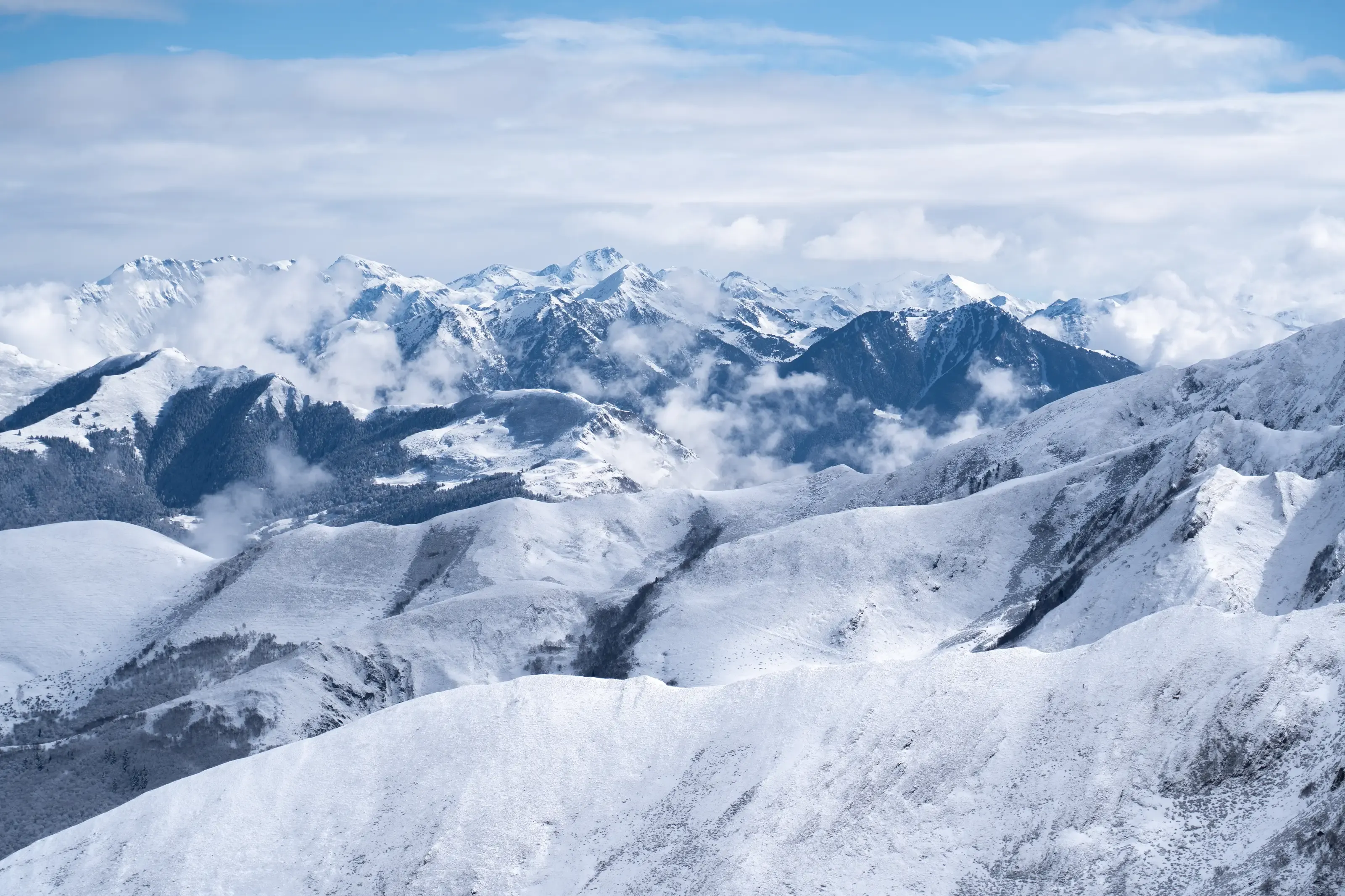 Panorama des sommets enneigés des Pyrénées depuis les hauteurs de Peyragudes, avec des crêtes montagneuses baignées de lumière et des nuages.