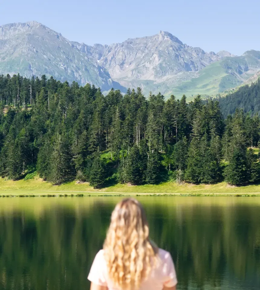 Mujer de espaldas observando una vista panorámica con montañas bosques y agua