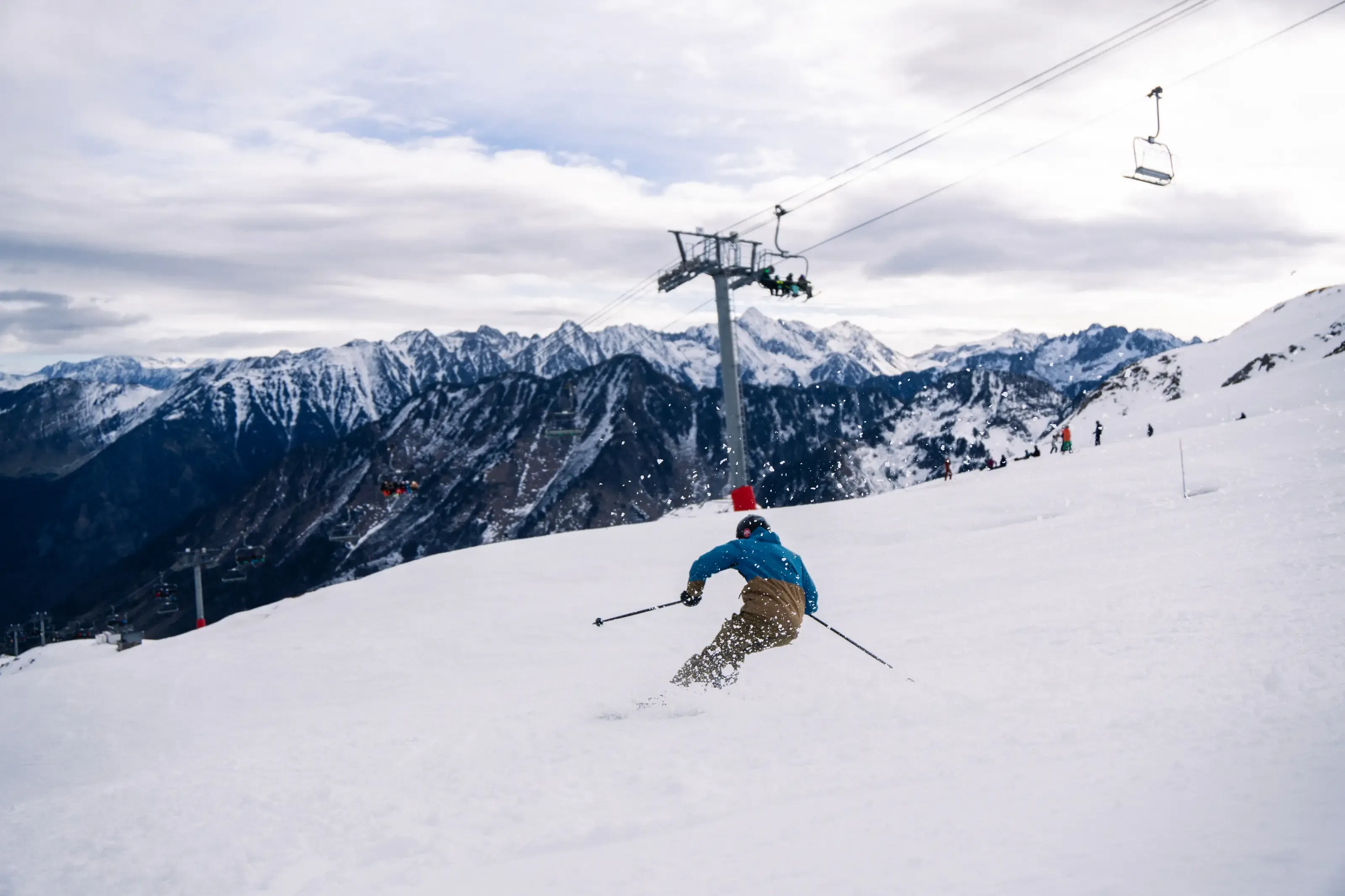 Skieur en virage sous un télésiège à Cauterets, face aux sommets enneigés des Pyrénées