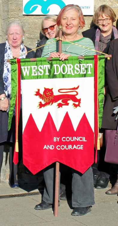 Councillor Karen Hunt holding a replica of the West Dorset Women's Suffrage Society banner, made by Holly Miller from a sketch by the suffragist banner-maker Mary Lowndes