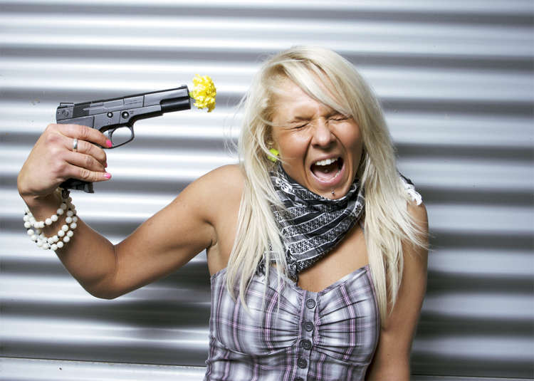 A blonde woman with a fake plastic gun with a yellow flower on the barrel. (Image - CC 2.0 bit.ly/3mFFk1R Beercha Unchanged)