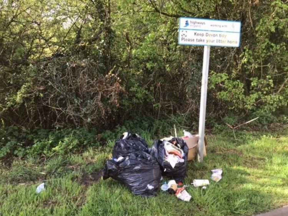 Litter dumped on a roadside at the foot of a Highways England 'Keep Devon tidy' sign