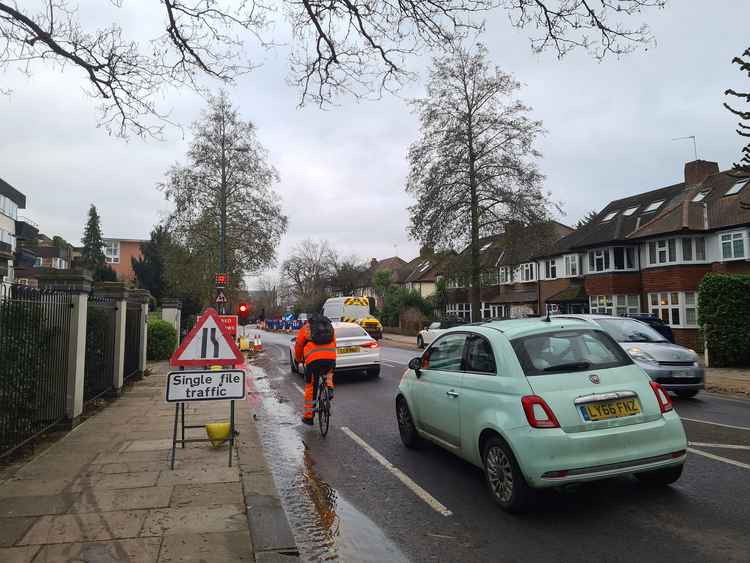 Drivers and a cyclist wait for the temporary lights to go green