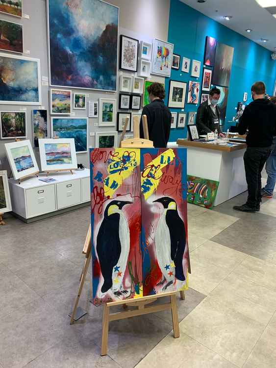 An art gallery featuring two side-by-side paintings of penguins on a red, blue and yellow background
