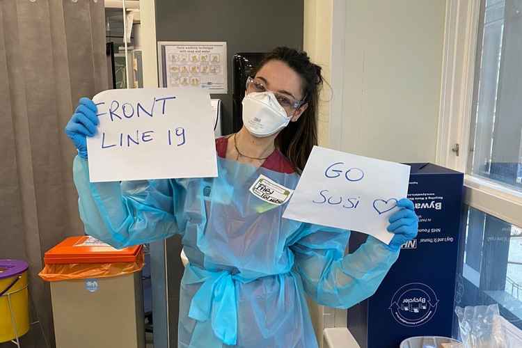 A frontline worker in scrubs holds up posters supporting Susi's challenge / Photo: Susi Halley