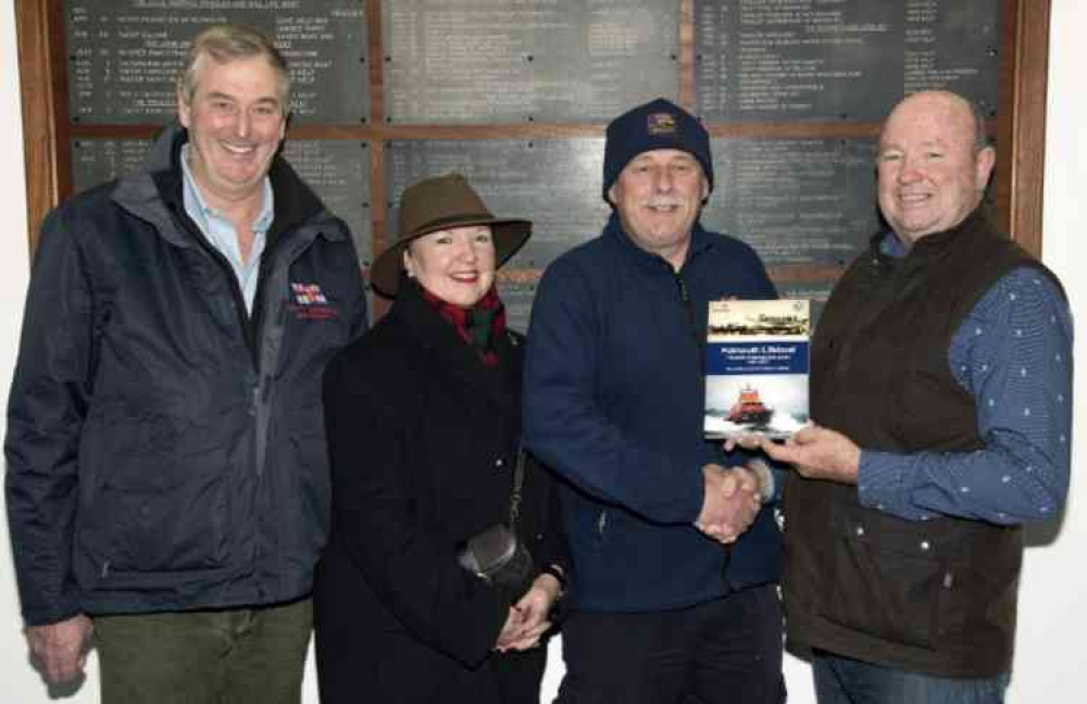 Falmouth RNLI Coxswain Jonathon Blakeston presenting Chris Lloyd with a signed copy of the station book produced in 2017 to commemorate the station's 150th anniversary with Jane Lloyd and Lifeboat Operations Manager Nick Lewis to the left.