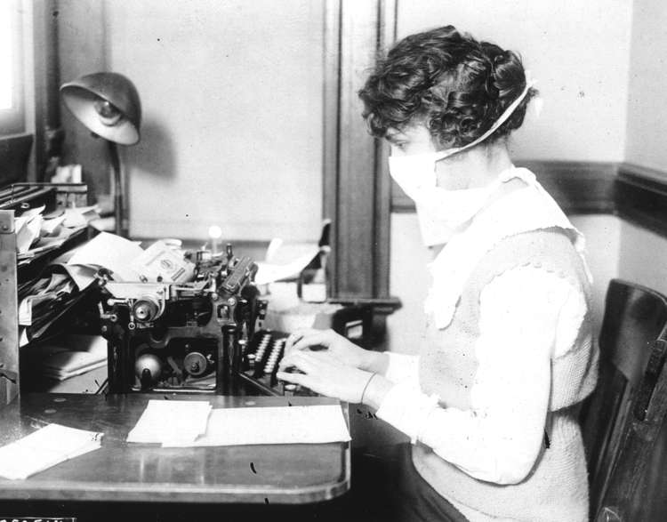 A typist wears mask while working at her office desk, during the influenza epidemic, 1918. Credit: Getty Images.