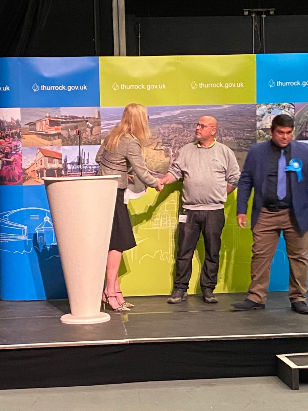 Victorious Cllr John Allen has a handshake for CEO Lyn Carpenter, while Tory candidate Jordan Ali watches on. 