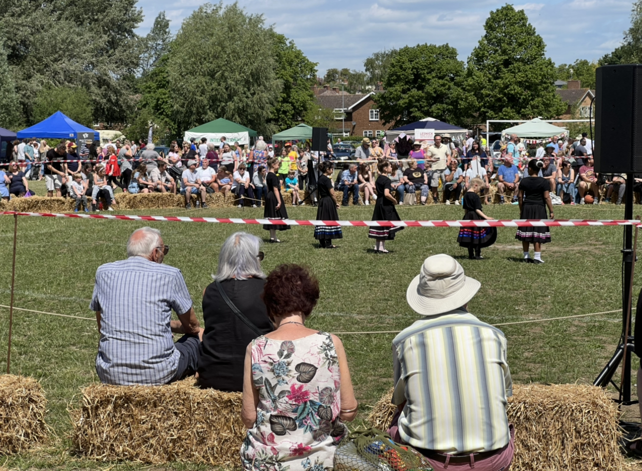 Crowds sit on bales of hay and watch dancers at the Walsworth Festival. CREDIT: @HitchinNubNews 