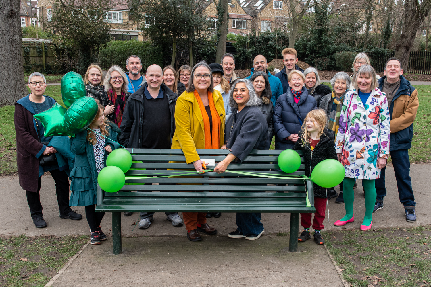 Julie Bentley, chief executive of Samaritans (centre, with scissors) assisted to her left by Heena Johnson, director of Ealing, Hammersmith & Hounslow Samaritans cuts the ribbon to formally open the bench in Lammas Park, Ealing to celebrate 50 years of Samaritans in West London.