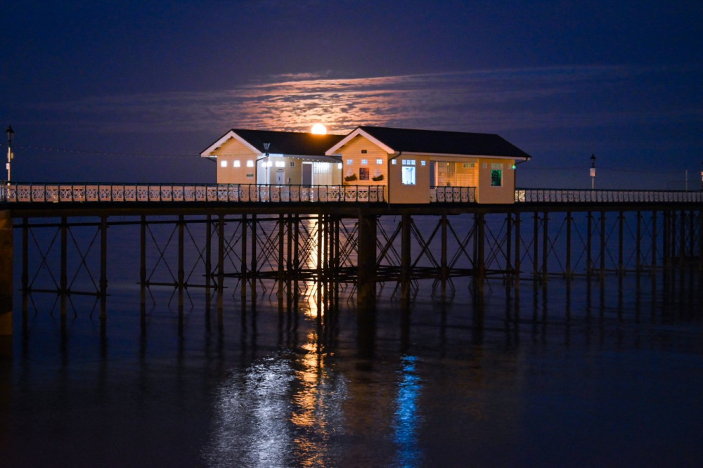 Shot from the prom, the moon rises above the pier huts