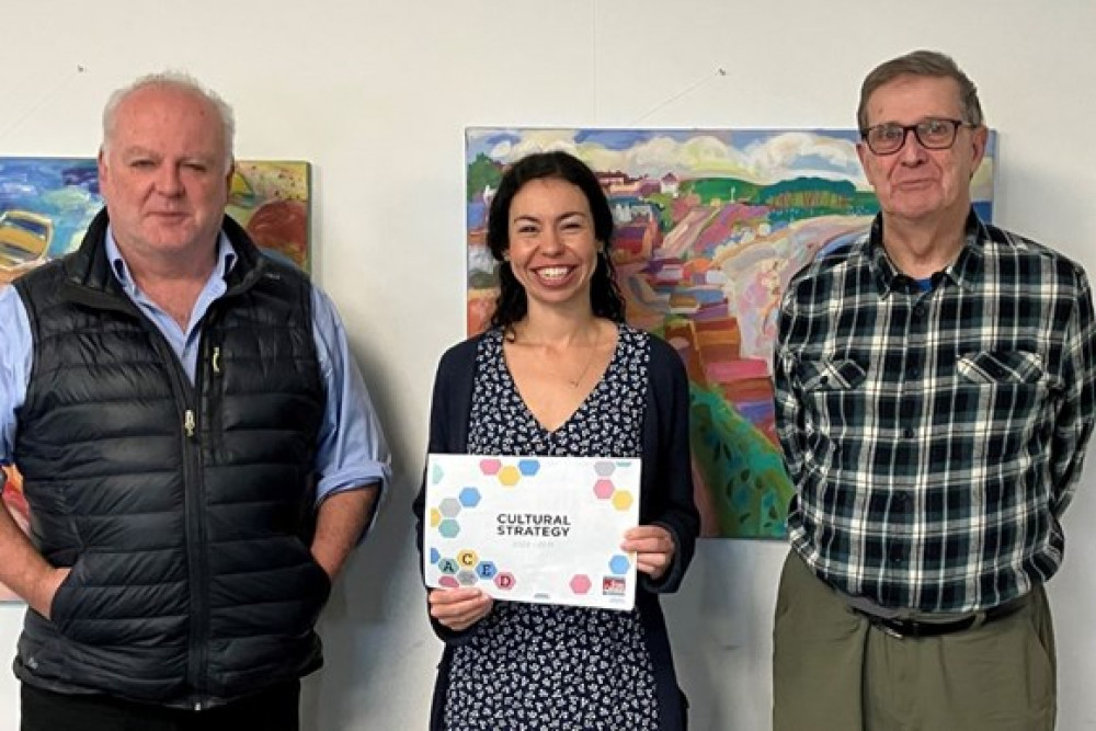 Councillor Paul Arnott with EDDC’s new cultural producer Sarah Elghady and Cllr Nick Hookway. The paintings in the background are by artist Michael Buckland. (Credit: EDDC).