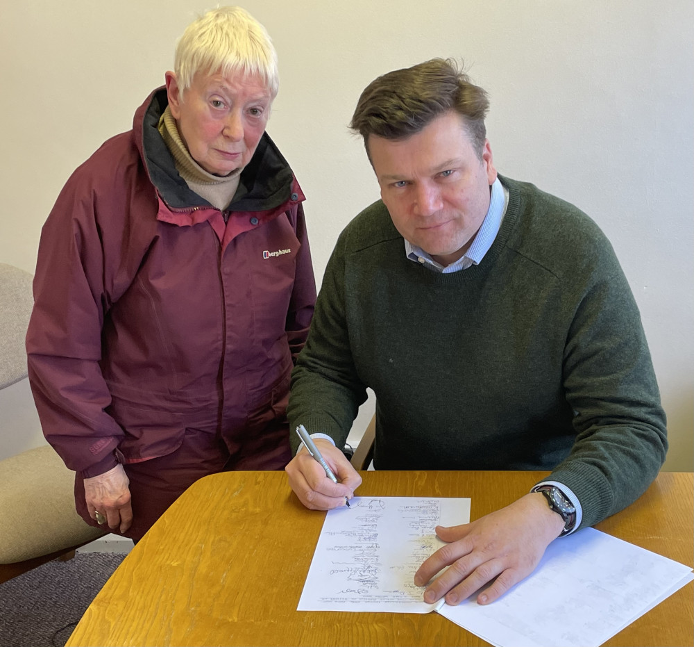 Beryl Fricker watches MP James Heappey sign her petition in Wells Town Hall  