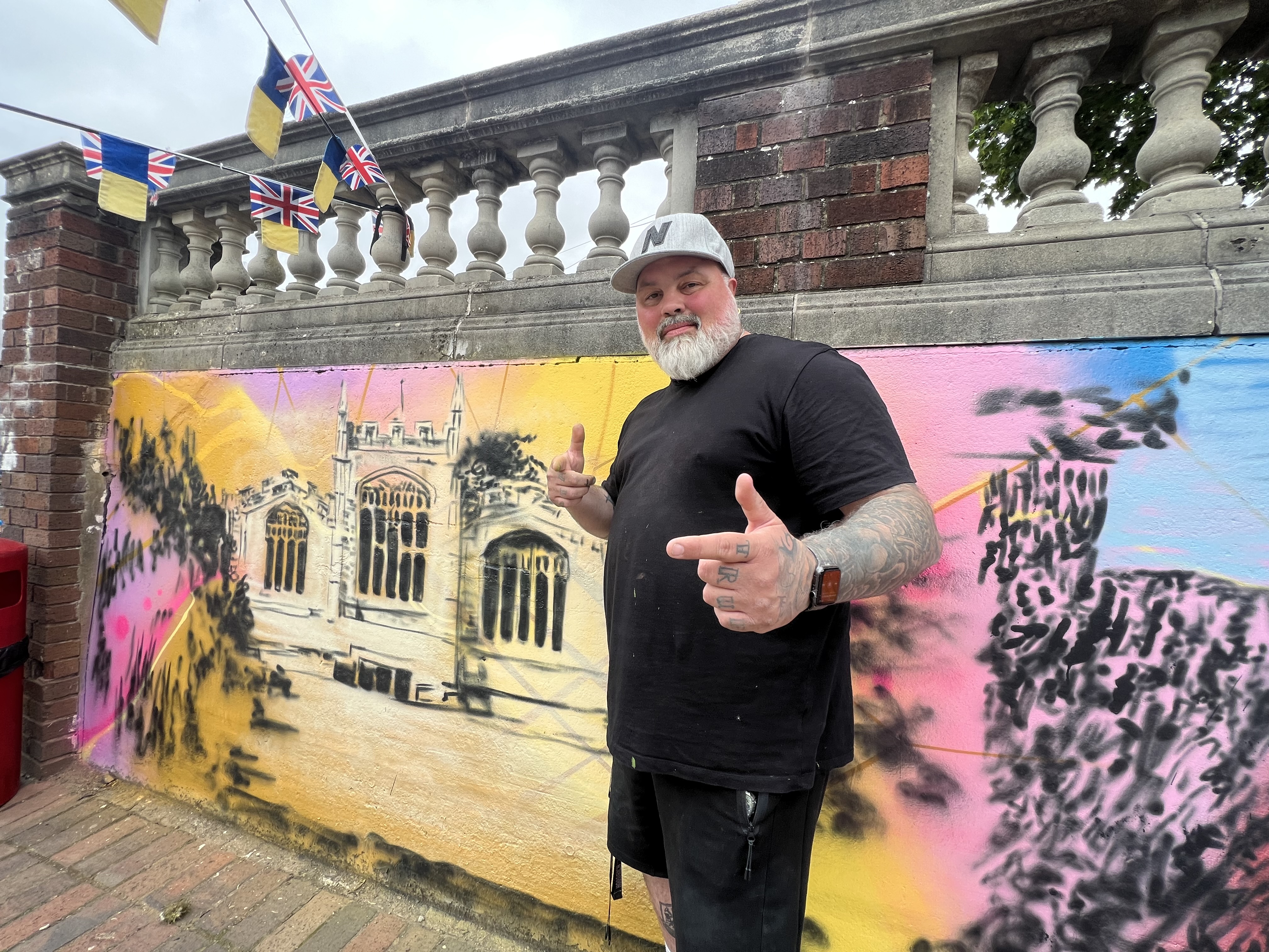 Hitchin Street Art icon Mr Meana in front of the incredible mural in Hitchin market that he is currently working on. CREDIT: Hitchin Nub News 