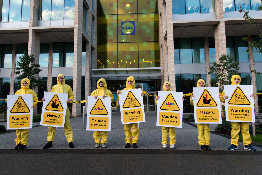 Activists in hazmat suits stand outside Lidl HQ. (Photo: The Humane League UK and Open Cages)