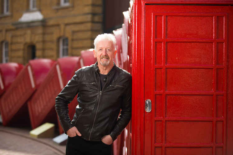 A photo of David Mach RA standing next to the toppling red telephone boxes on Old London Road / Credit: Kingston First