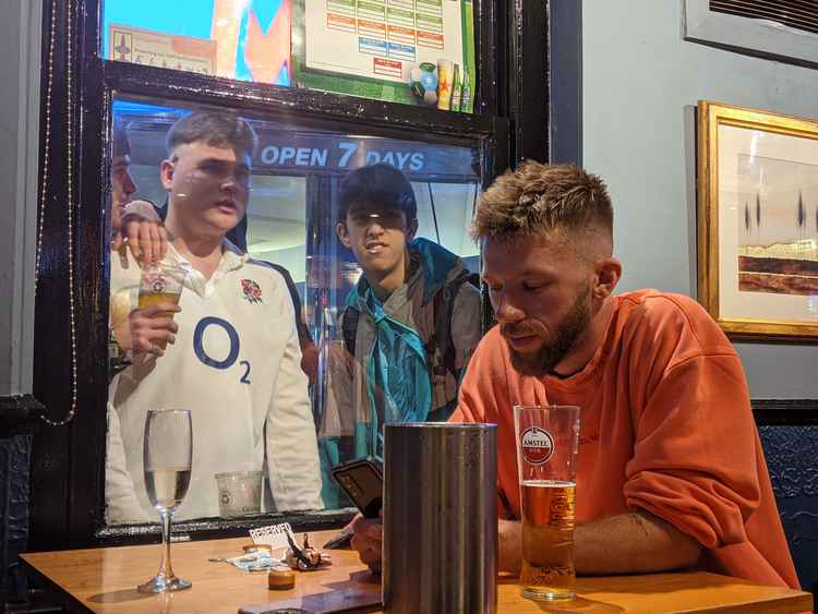 An England fan at the pub looks down in despair as others outside show their disappointment (Credit: Nub News)