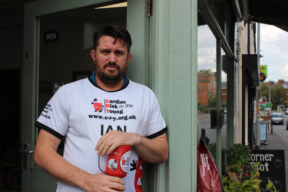 Ian Heslop, outside The Corner Plot, with a charity pot and shirt for Cardiac Risk in the Young. (Image - Macclesfield Nub News) 