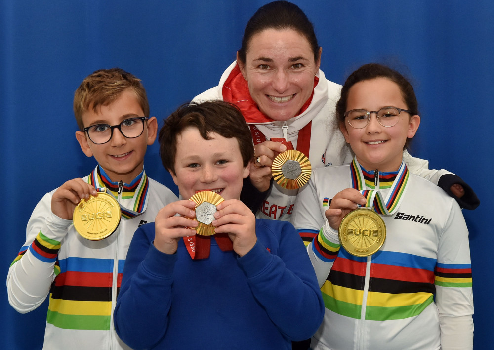 Dame Sarah is pictured with King's Macclesfield School Captains Luca Williams and Olivia Saxton, with Charlie Storey in the middle, wearing the two Paris Gold Medals and the rainbow jerseys and Gold medals from the World Championships. 