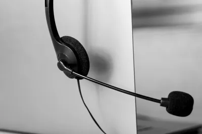 A call-centre headset with its microphone boom extended, hanging on the edge of a desk partition.