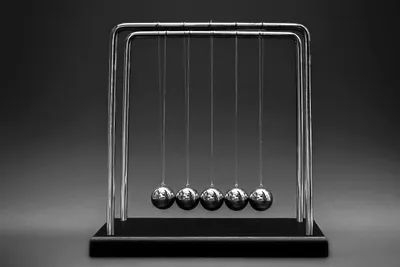 Abstract Numr artwork: five identical polished steel spheres hanging in a row from a chrome frame, a Newton's cradle at rest.