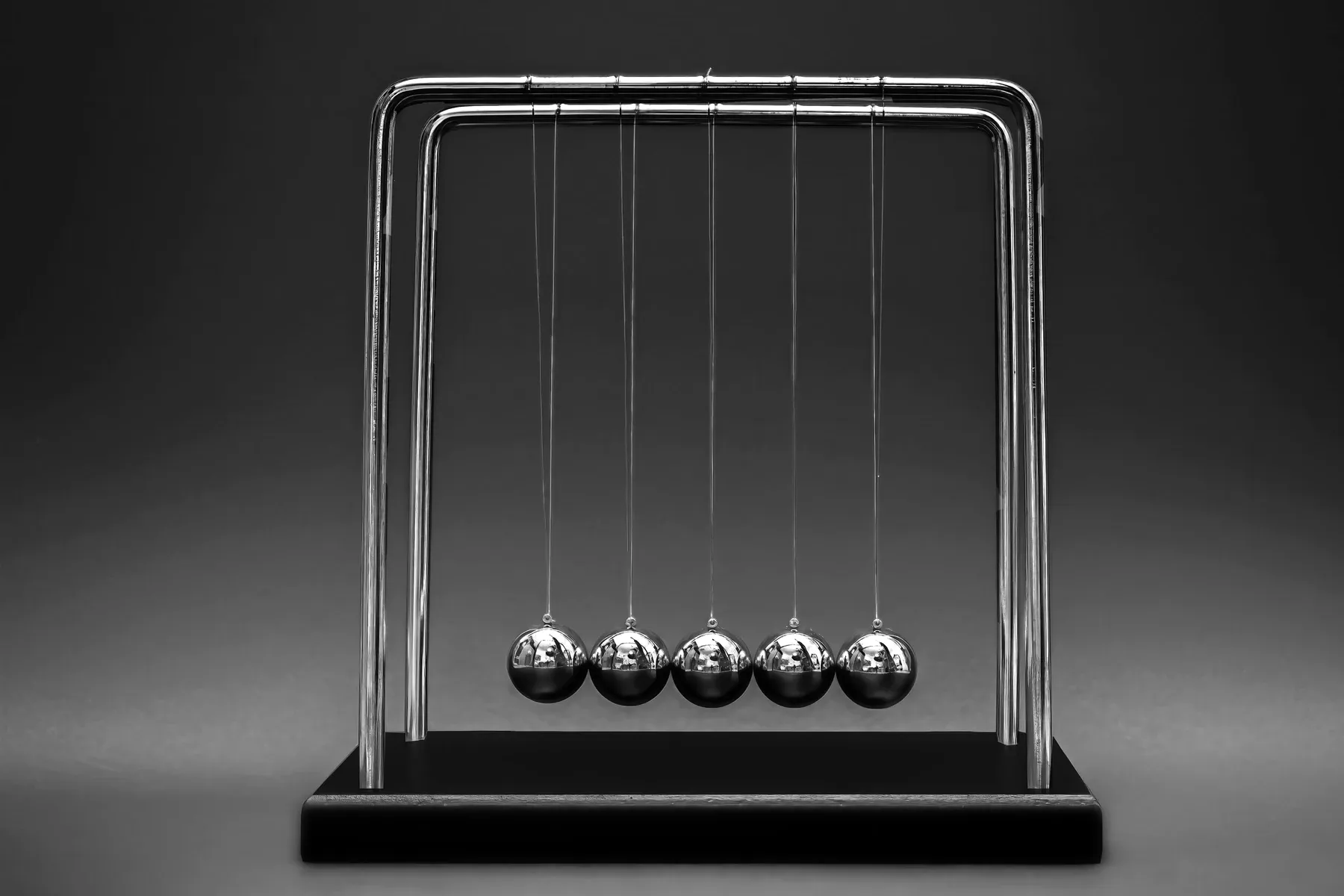 Abstract Numr artwork: five identical polished steel spheres hanging in a row from a chrome frame, a Newton's cradle at rest.