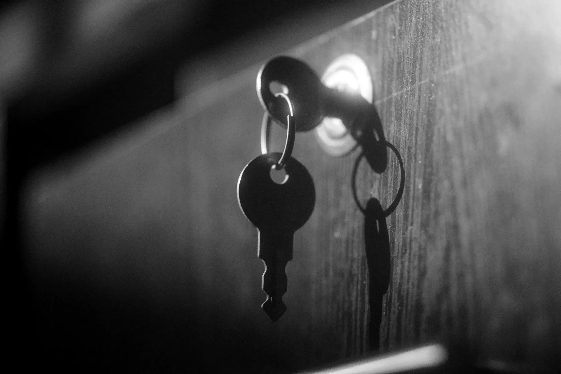 A key hanging from a lock in a dark wooden door, lit from one side.