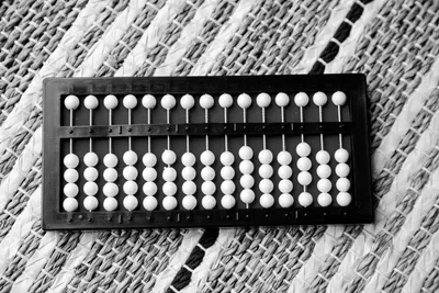 A wooden abacus lying on a woven mat, its upper row of beads raised and its lower rows counted across.