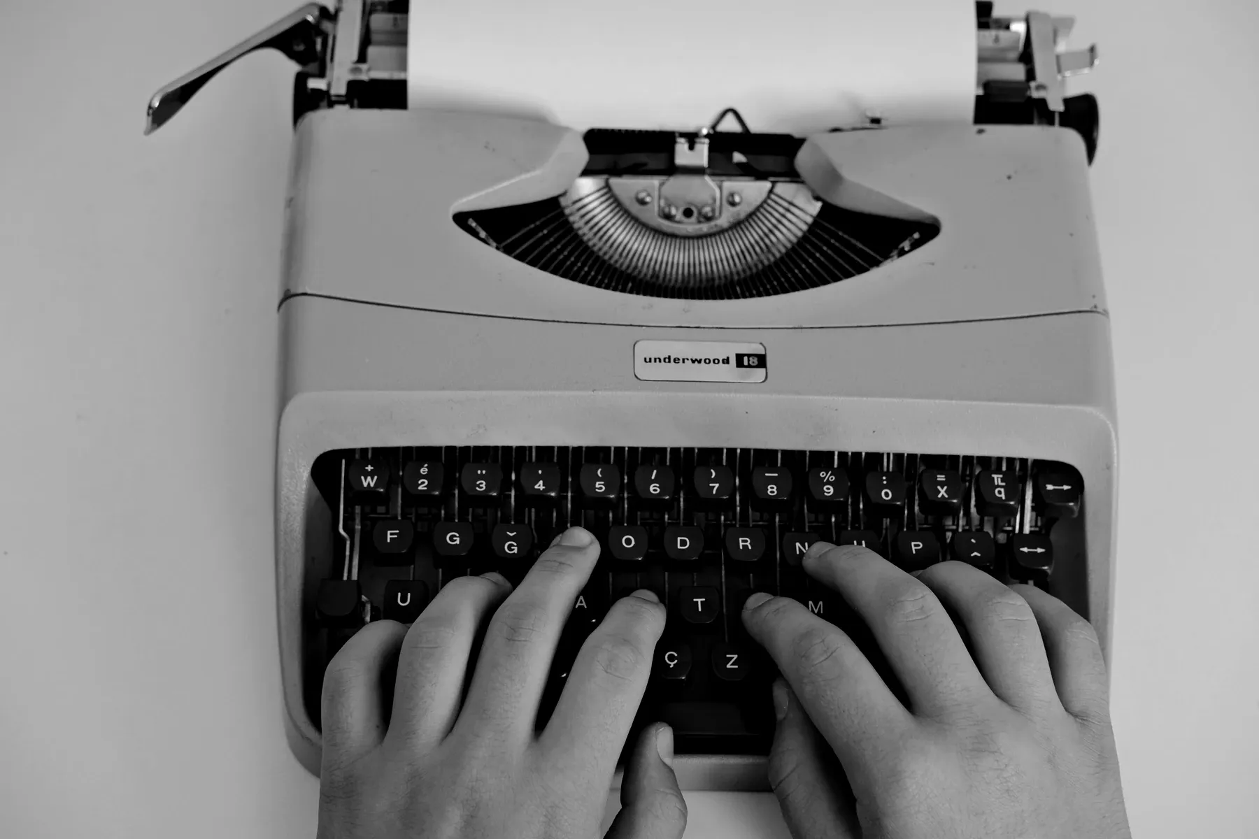 Overhead view of two hands typing on a manual Underwood typewriter, a sheet of paper rolled into the carriage.