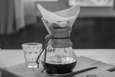 Abstract Numr artwork: a glass pour-over brewer, wet coffee grounds resting in the filter cone above and a shallow pool of brewed coffee pooled in the base below.