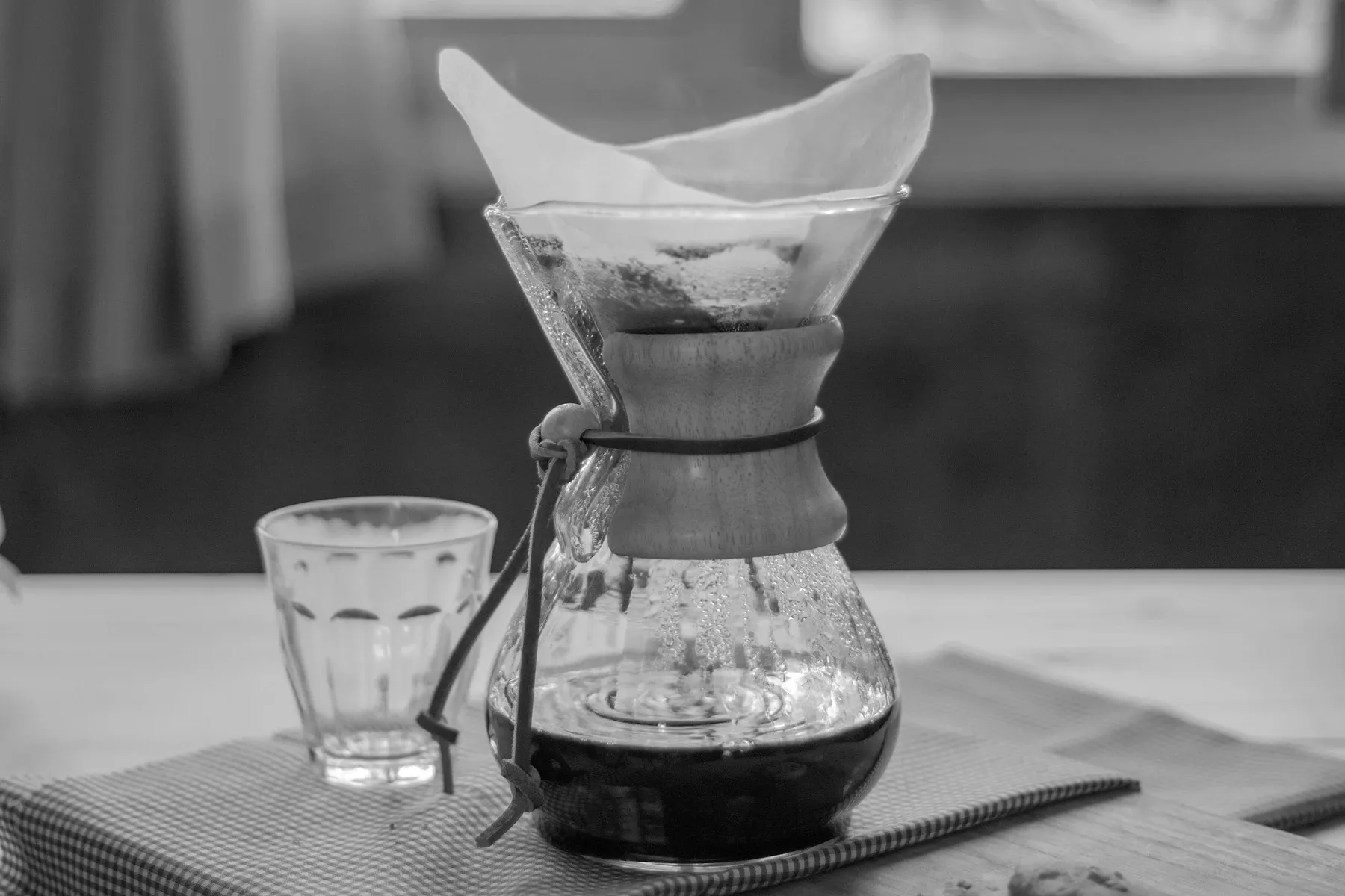Abstract Numr artwork: a glass pour-over brewer, wet coffee grounds resting in the filter cone above and a shallow pool of brewed coffee pooled in the base below.