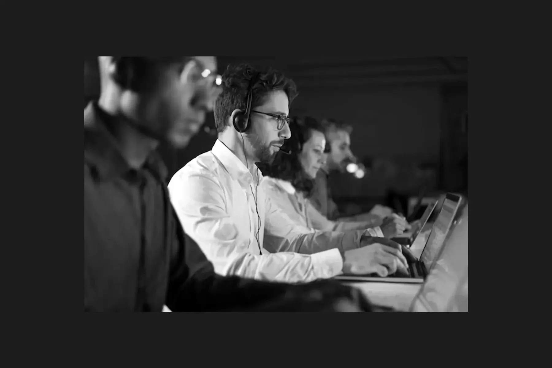 A row of contact-centre agents in headsets working at their screens, the nearest in focus and the rest falling away down the line.