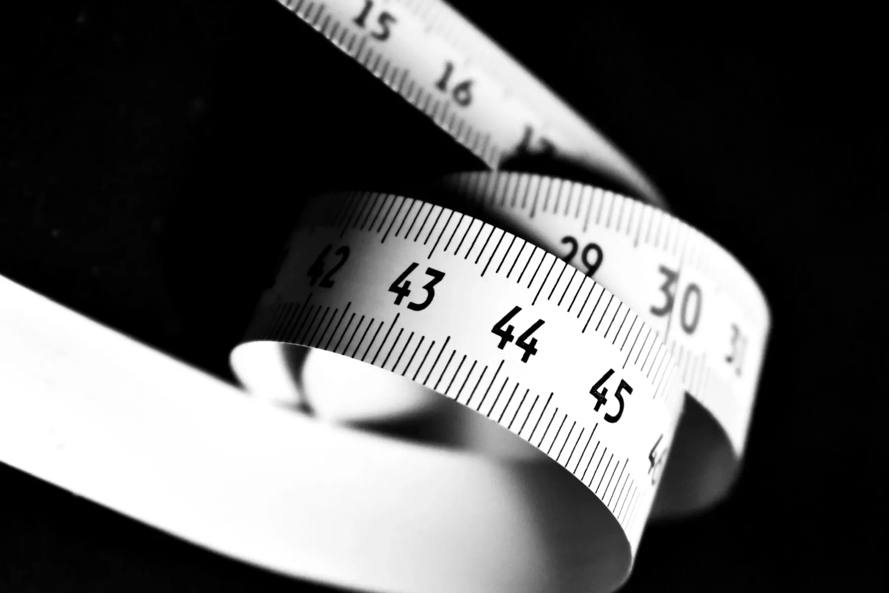 A curled measuring tape on a black background, its graduations and numbers running along the edge.