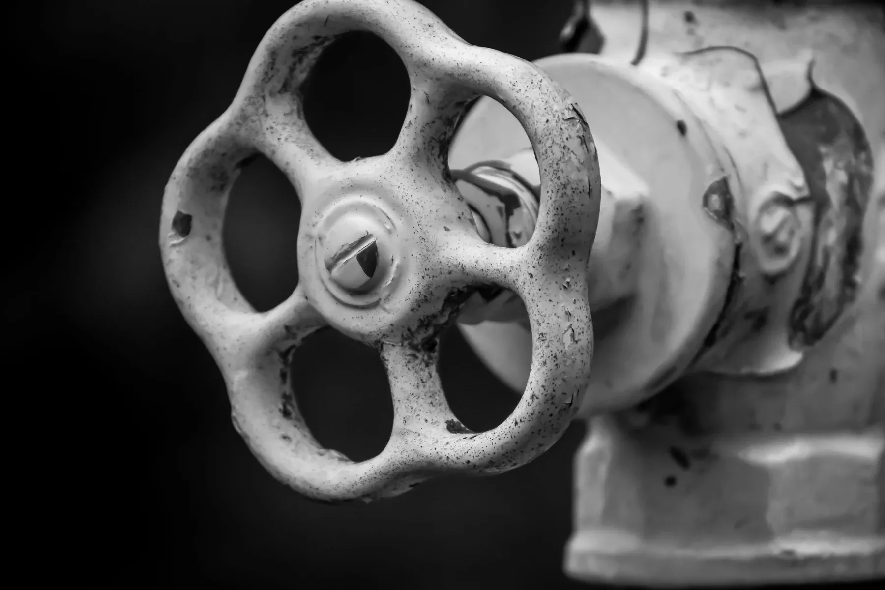 A heavy valve wheel on an old pipe, lit from one side.