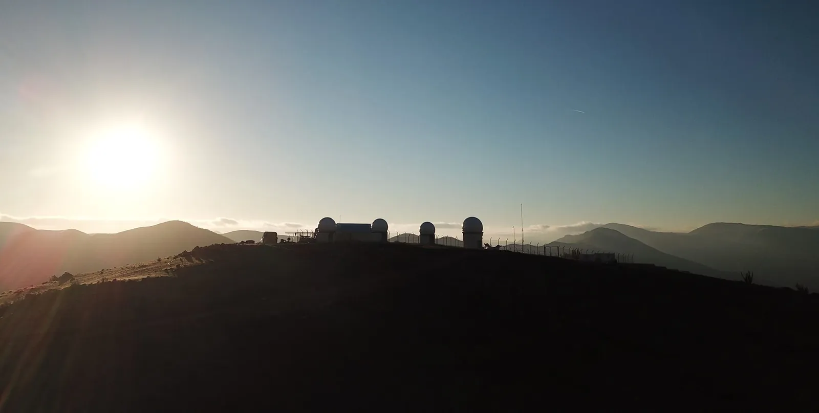 The domes and the fenced compound on the ridge at sunset, hills and a sea of clouds behind